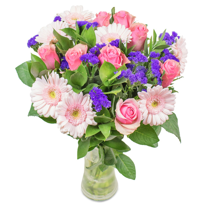 This luminous bouquet, artfully arranged in a simple glass vase by Blackwall florists, commands attention amid a crisp white backdrop. At its core, seven to nine pink roses stand in various stages of blossom, their elegant spiral petals capturing the refined beauty often seen in the gardens of Poplar Dock. These are gracefully complemented by five to seven pale pink Gerbera daisies, large and cheerful, their soft petals radiating from creamy centres and bringing to mind the open, fresh spaces of Blackwall's riverside walks. Interwoven among the main blooms, vivid purple accents of statice offer a playful textural contrast, enhancing the composition's vibrancy much like colourful houseboats along the Thames. Deep, green foliage adds fullness and a sense of abundance, its richness evoking the refreshment of nearby Millennium Park. The clear vase allows the stems and water to be visible, highlighting freshness and the attention to detail Blackwall Flowers brings to every local delivery. Suitable for birthdays, office celebrations, or warm family gatherings in E14, this pink-centric arrangement evokes joy and heartfelt connection, subtly reflecting the community spirit of Blackwall.